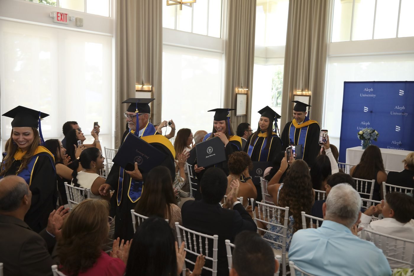 Graduates processing through the hall as families and guests applaud during the Aleph University 2026 commencement ceremony.